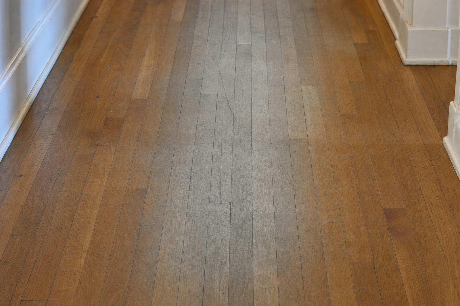 A greyed, worn traffic path down the middle of an oak hallway floor